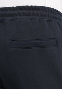 Navy joggers with a textured waistband and a back pocket featuring a ribbed edge. Made from soft, comfortable fabric.