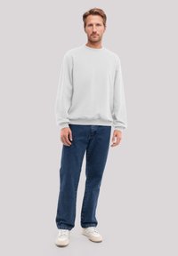White crewneck sweatshirt with long sleeves, paired with blue straight-leg jeans and white sneakers. Simple, comfortable design.