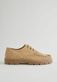 Zapatos de ante marrón con cordones, punta redonda, suela de goma y detalles de costura. Presenta ojales de metal y una superficie texturizada.