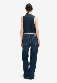 Džínová crop top s pevným designem, v kombinaci s širokými džíny; oboje v tmavě modré s viditelným šitím a zadními kapsami.