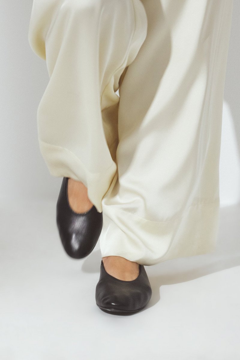 Zwarte leren ballerina's met een ronde neus, gecombineerd met vloeiende crème-kleurige broek. Gladde textuur, eenvoudig en klassiek ontwerp.