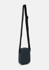Piccolo borsa a tracolla rettangolare in materiale blu scuro con una texture liscia, dotata di una tracolla nera regolabile e chiusura con zip.