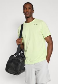 T-shirt Nike vert citron, logo noir sur la poitrine, assorti à un short gris clair. Sac de sport noir foncé avec panneau en mesh et sangle.