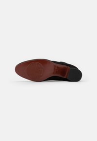 Scarpa in suede nera con punta arrotondata e suola in pelle marrone. La suola presenta un motivo testurizzato per la presa e un dettaglio del marchio.