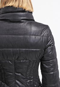 Schwarze Daunenjacke mit glänzender, strukturierter Oberfläche. Verfügt über horizontale Steppnähte und einen hohen Kragen, zeigt eine taillierte Silhouette.
