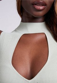 Haut en maille côtelée vert clair avec un col montant, présentant de grandes découpes au niveau de la poitrine et du dos, mettant en valeur une texture lisse et une coupe ajustée.