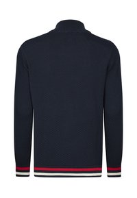 Marinblå stickad tröja med ett texturerat mönster, hög krage och ribbade ärmslut som har röda, vita och blå ränder vid fållen.