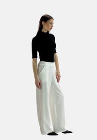 Maglione aderente nero a girocollo, pantaloni bianchi a gamba larga con tasche laterali, tessuto liscio, hardware minimal, silhouette elegante, abbinato a scarpe nere a punta.