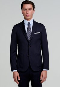 Blazer azul marino con dos bolsillos frontales, dos botones y solapas con muesca. Combinado con una camisa de color azul claro y una corbata con patrones. Diseño limpio y ajustado.
