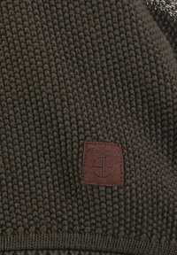 Tessuto a maglia verde scuro con una superficie testurizzata, caratterizzato da un'etichetta in pelle marrone con "KEY LARGO" impresso in lettere maiuscole.