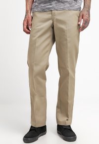 Khaki bukser med lige ben, lavet af glat stof. Har flad front og sidelommer, samt sorte sneakers.