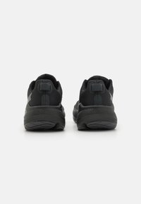 Scarpe sportive nere con tomaia texturizzata, collo imbottito e suola spessa. Presentano un logo discreto e un tassello sul tallone per facilitarne l'indossamento.