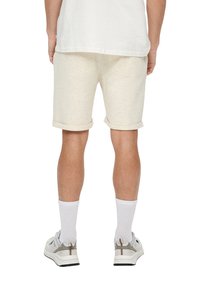 Beige Baumwollshorts mit umgeschlagenen Säumen, getragen mit weißen Socken und grauen Turnschuhen, von hinten gezeigt.