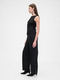 Top preto canelado sem mangas com um decote alto, combinado com jeans pretos de perna larga. O modelo usa botas de tornozelo pretas e pontudas. Design simples.