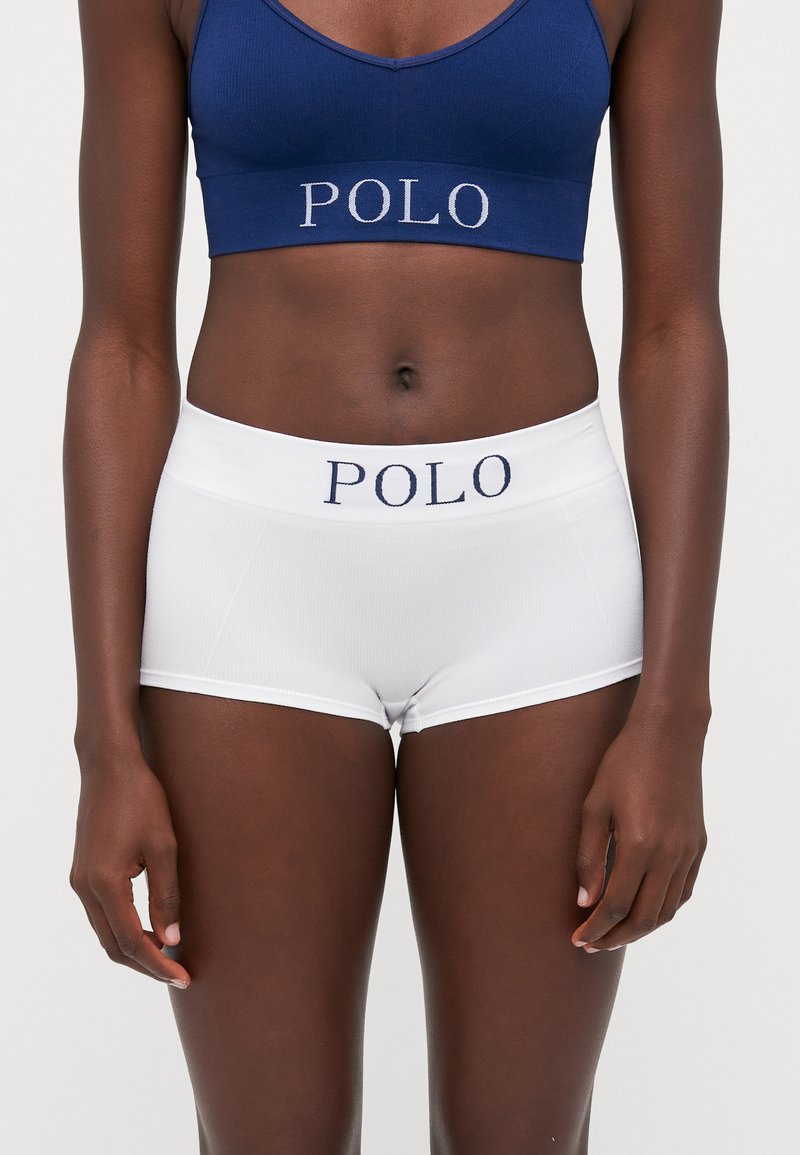 Zilas kokvilnas sporta krūšturis un baltas hipster šortas ar zilu "POLO" logo uz jostas, ar gludu tekstūru un pieguļošu dizainu.