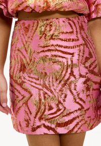 Minifalda rosa corta con un patrón texturizado de rayas doradas y rojas. El material tiene un acabado brillante con una sutil textura en relieve.