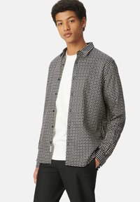 Zwart-wit gestreept shirt met een kraagontwerp, lange mouwen en een relaxed fit, gedragen over een wit T-shirt met ronde hals.