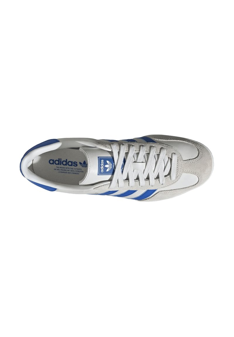 Chaussure de sport blanche avec des détails en suède gris et trois bandes bleues, dotée d'un système de laçage et d'une semelle intérieure avec logo.