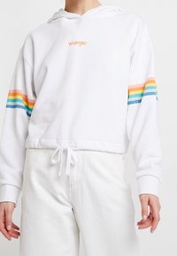 Felpa corta bianca con logo "Wrangler", presenta strisce arcobaleno sulle maniche, orlo con cordino, vestibilità comoda e texture in tessuto morbido.