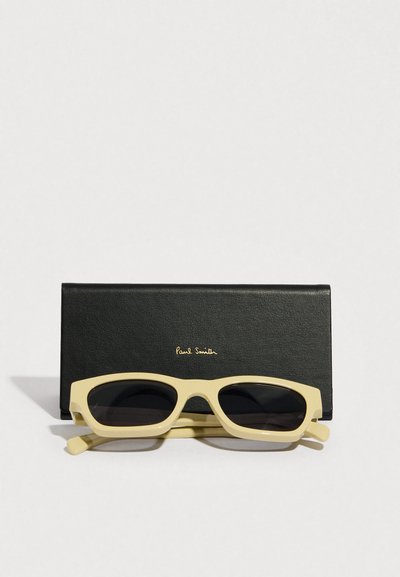 Gafas de sol rectangulares amarillas con lentes oscuras, colocadas en un estuche de cuero negro con un logo en relieve dorado.