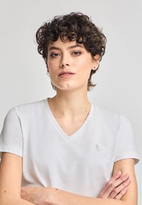 Vit bomullströja med V-ringning och korta ärmar. Har en liten broderad logga på bröstet. Slät textur.