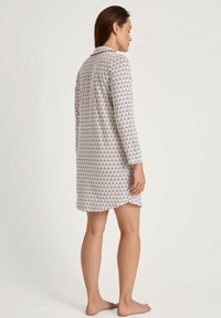 Vestito da notte a maniche lunghe in tessuto bianco e stampato, con colletto, dettagli con bottoni e orlo leggermente curvo. Texture morbida.