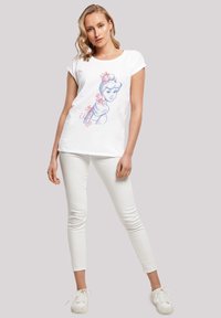 Hvit bomull T-skjorte med et blått og rosa illustrert design av en kvinne med blomster i håret, parret med hvite skinny bukser og hvite sneakers.