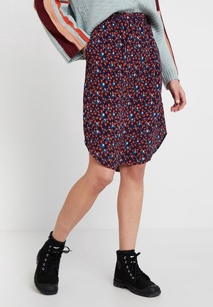 Personne portant une jupe fleurie marine longueur genou, un pull bleu clair avec des manches rayées multicolores, et des bottines noires à lacets.