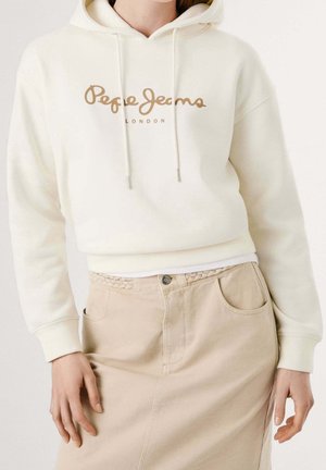 Femme portant un sweat à capuche crème avec le texte "Pepe Jeans London" et une jupe beige taille haute avec poches avant et ceinture tressée.