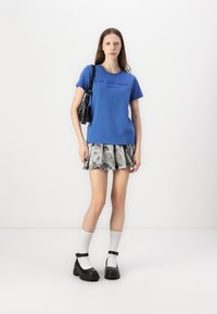 Mėlyna medvilnė t-shirt su trumpomis rankovėmis ir grafiniu spaudiniu, derinama su pilka klostuota sijonu. Juodi masyvūs aukštakulniai batai ir balti kulkšnies kojinės.