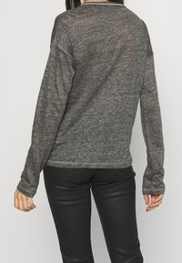 Maglione grigio a maniche lunghe realizzato in un tessuto leggero e texture. Presenta un collo rotondo e cuciture a contrasto lungo gli orli.