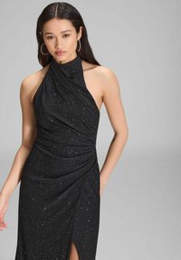 Schwarzes Neckholderkleid aus strukturiertem Stoff mit silbernen Sprenkeln, Drapierung und einem Oberschenkel-Spitzenaufschlag auf einer Seite.