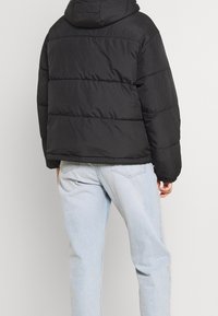 Czarna puchowa kurtka z kapturem, z pikowanym wzorem, ściągaczami na rękawach i lekko skróconym dołem, zestawiona z jasnoniebieskimi dżinsami.