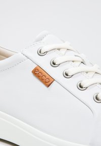 Weiße Leder-Sneaker für die Freizeit mit weißen Schnürsenkeln, Metallösen und einem kleinen braunen Lederetikett mit geprägtem Markennamen.