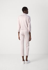 Lichtroze, getailleerde blazer en bijpassende cropped broek. Glad materiaal met een kraag, mouwlengte tot de elleboog en subtiele naaddetails aan de achterkant.