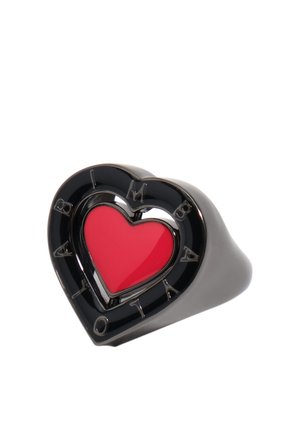 Anillo negro con forma de corazón, con un corazón rojo en el centro y la inscripción "BALMAIN" alrededor del borde exterior.