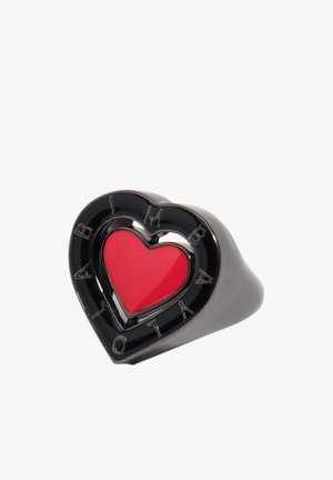 Črni prstan v obliki srca z rdečim srcem v sredini in vgraviranim napisom "BALMAIN" okoli zunanjega roba.