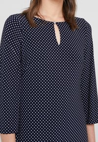Námořnická modrá blůza s bílými puntíky, s výstřihem ve tvaru klíčové dírky a tříčtvrtečními rukávy. Vyrobena z lehkého, texturovaného materiálu.
