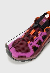 Trailrunning-Schuh mit einem Obermaterial aus Mesh in lila, schwarz und orange, einer verstärkten Zehenschutzkappe und elastischen Schnürsenkeln für einen sicheren Sitz.
