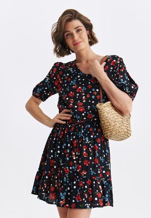 Sukienka kwiatowa z czarnej tkaniny z czerwonymi, niebieskimi i białymi wzorami; krótkie bufiaste rękawy, dekolt w serek oraz taliowana w pasie. W zestawie pleciona torba.