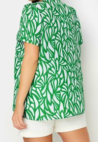 Green and white short-sleeve top featuring a leaf pattern, made of lightweight fabric, with a loose fit and rounded neckline.