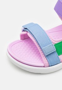 Sandalias en rosa, azul y verde con una plantilla texturizada, correas ajustables y una suela de goma ligera con un borde blanco.