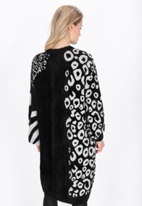 Črno-bela oversized jopica z fluffasto teksturo. Vsebuje mešanico živalskih vzorcev in črt. Dolgi rokavi, odprt sprednji dizajn.