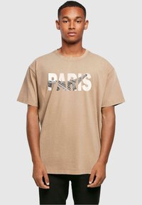 Tan bomull t-skjorte med en dristig grafikk "PARIS" med et teksturert Eiffeltårn-design, korte ermer og en avslappet passform.