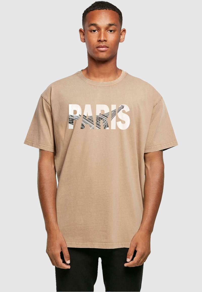 Tan väriinen puuvillapaita, jossa on boldi grafiikka "PARIS" ja teksturoitu Eiffel-torni -kuvio, lyhyet hihat ja rento istuvuus.