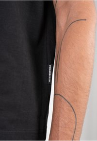 Czarny t-shirt z widoczną metką z napisem "ZABRONIONE". Materiał wydaje się miękki, o gładkiej fakturze i dopasowanym kroju.