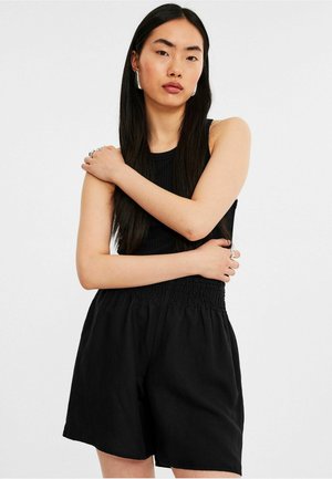 Svart ribbad ärmlös topp kombinerad med svarta smockade shorts. Tyget verkar lätt och ventilerande med en avslappnad passform.