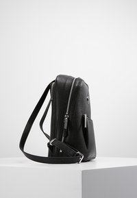 Czarny skórzany plecak o gładkiej fakturze, wyposażony w srebrne suwaki, boczną kieszeń oraz regulowany pasek. Kompaktowy i smukły design.