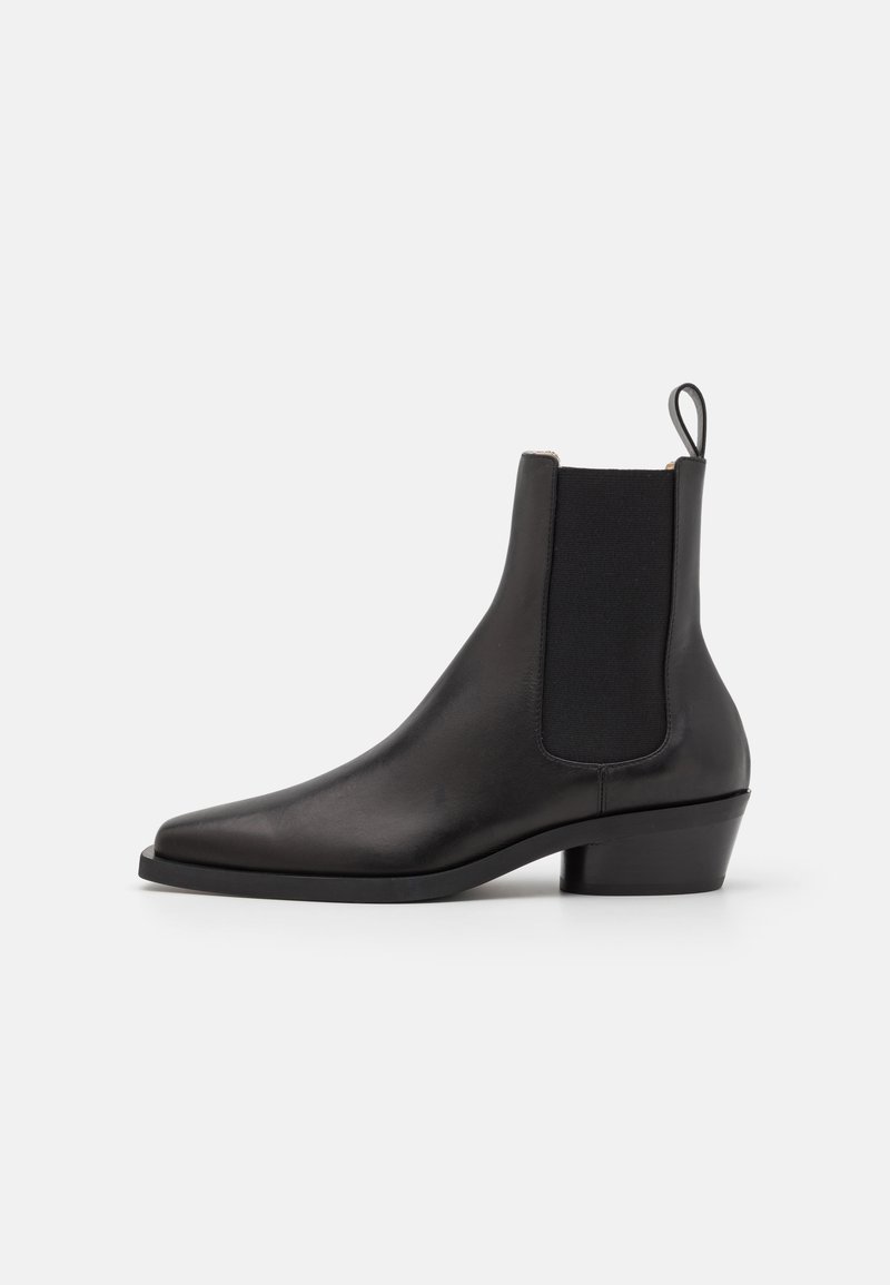 Botine Chelsea din piele neagră, cu vârf ascuțit, panouri elastice pe lateral și un toc mic, suprapus. Dispune de un tab pentru a fi îmbrăcate ușor.