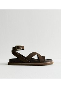 Sandalo in pelle marrone con cinturini incrociati, fibbia alla caviglia, suola piatta e suola testurizzata per una presa migliore. Design semplice e moderno.